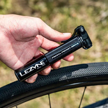 Load image into Gallery viewer, Hand holding a Lezyne Presta Pocket Drive Mini Pump near a bike tire with a blurred natural background